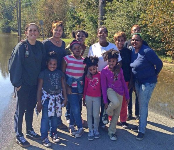 Members of the Solidarity caravan with Carolyn Dawson and Pastor Nancy Wade and Pastor Wade’s family at the edge of floodwaters in East Kinston, N.C. Ms. Dawson’s home is just beyond the trees.