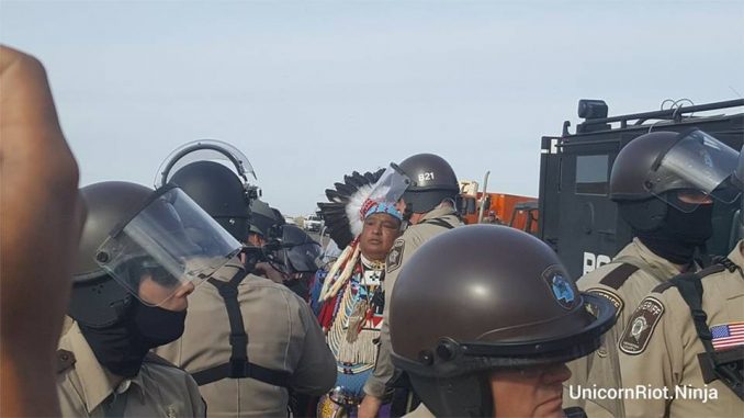 A Native elder in ceremonial dress, who was praying, is arrested by police and military at Oceti Sakowin Treaty Camp, Oct. 27.