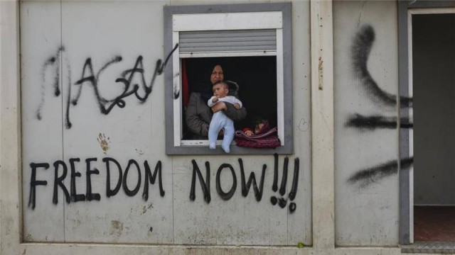 A woman with a child looks out from a container at a makeshift camp for refugees at the Greek-Macedonian border.